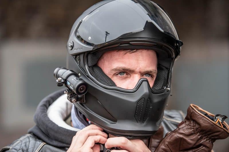 Man putting on black motorbike helmet with DC-1 Dual Lens Helmet Camera attached