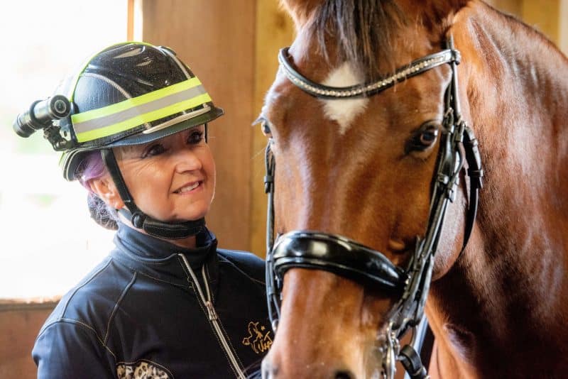 Woman smiling next to her horse whilst wearing DC-1 Dual Lens Helmet Camera