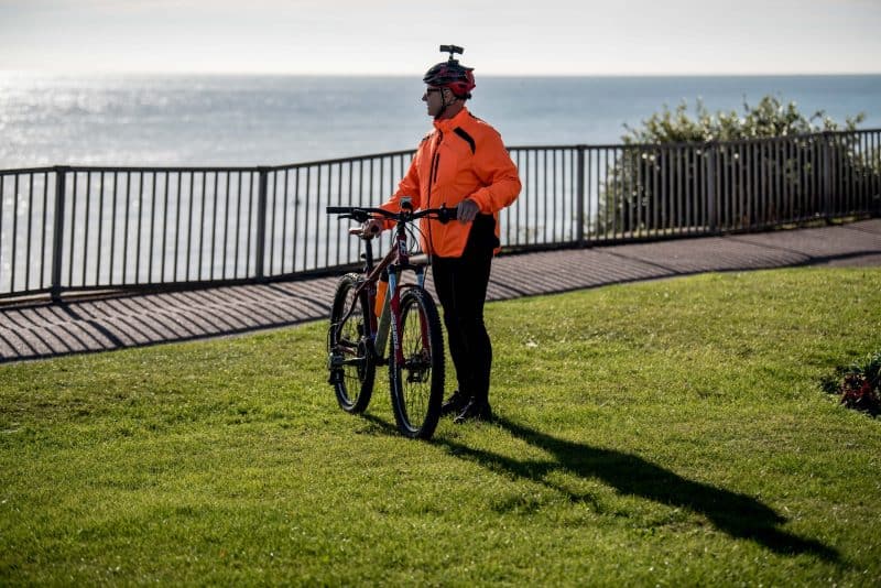 Man in orange cycling gear and wearing the DC-1 Dual Lens Helmet Camera