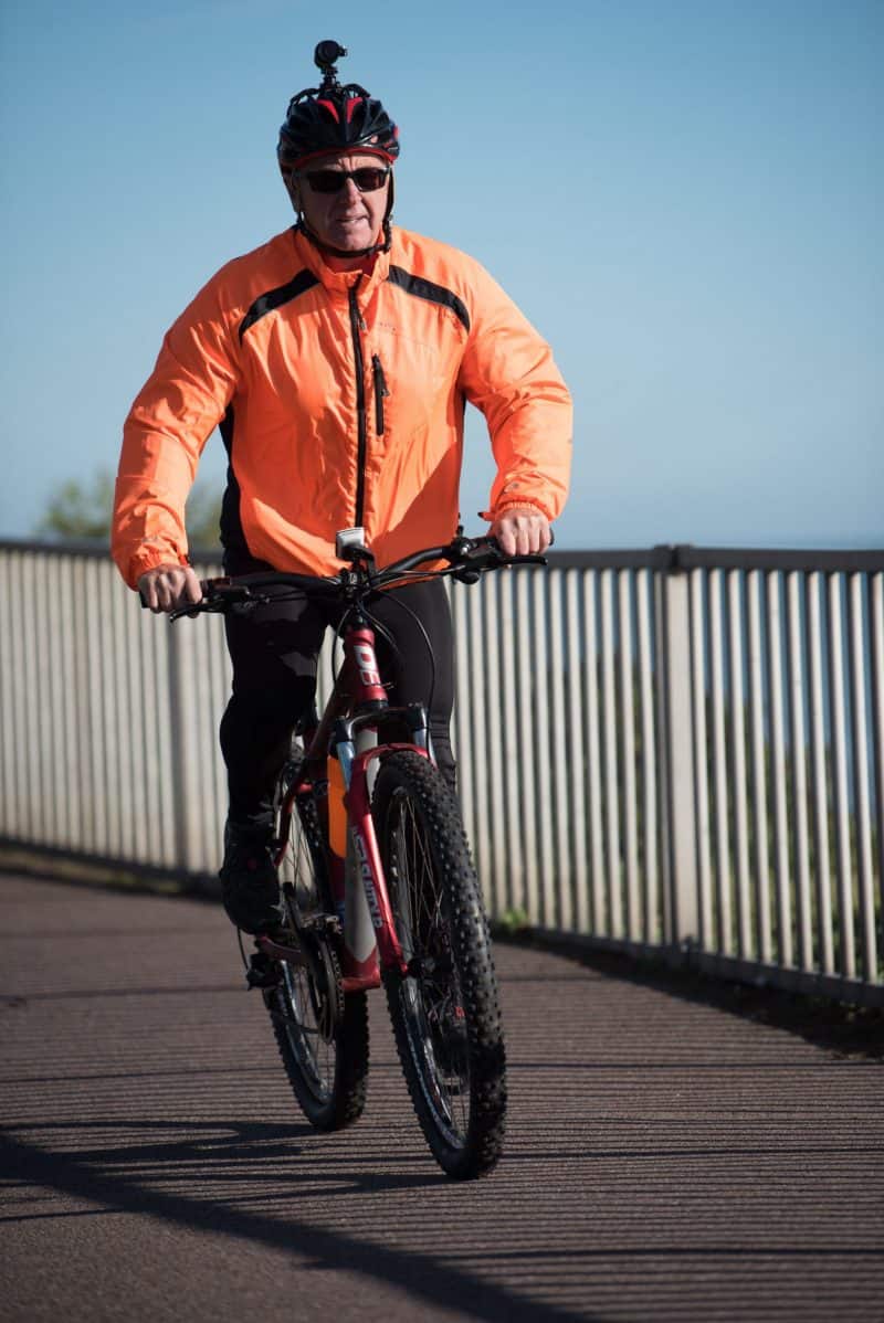 Man wearing orange cycling gear whilst riding his bike, with DC-1 Dual Lens Helmet Camera attached